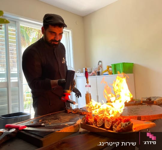 שף משתמש במבער להכנת מנות עם להבות על שולחן עץ